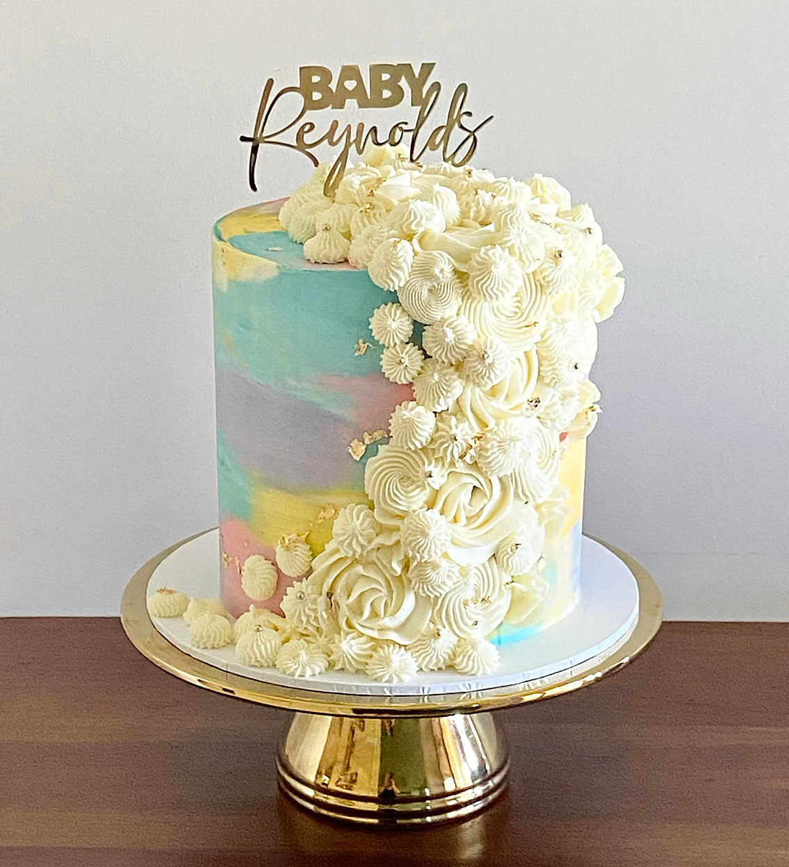 Gold Mirror Cake topper on a fancy cake reads "BABY Reynolds."