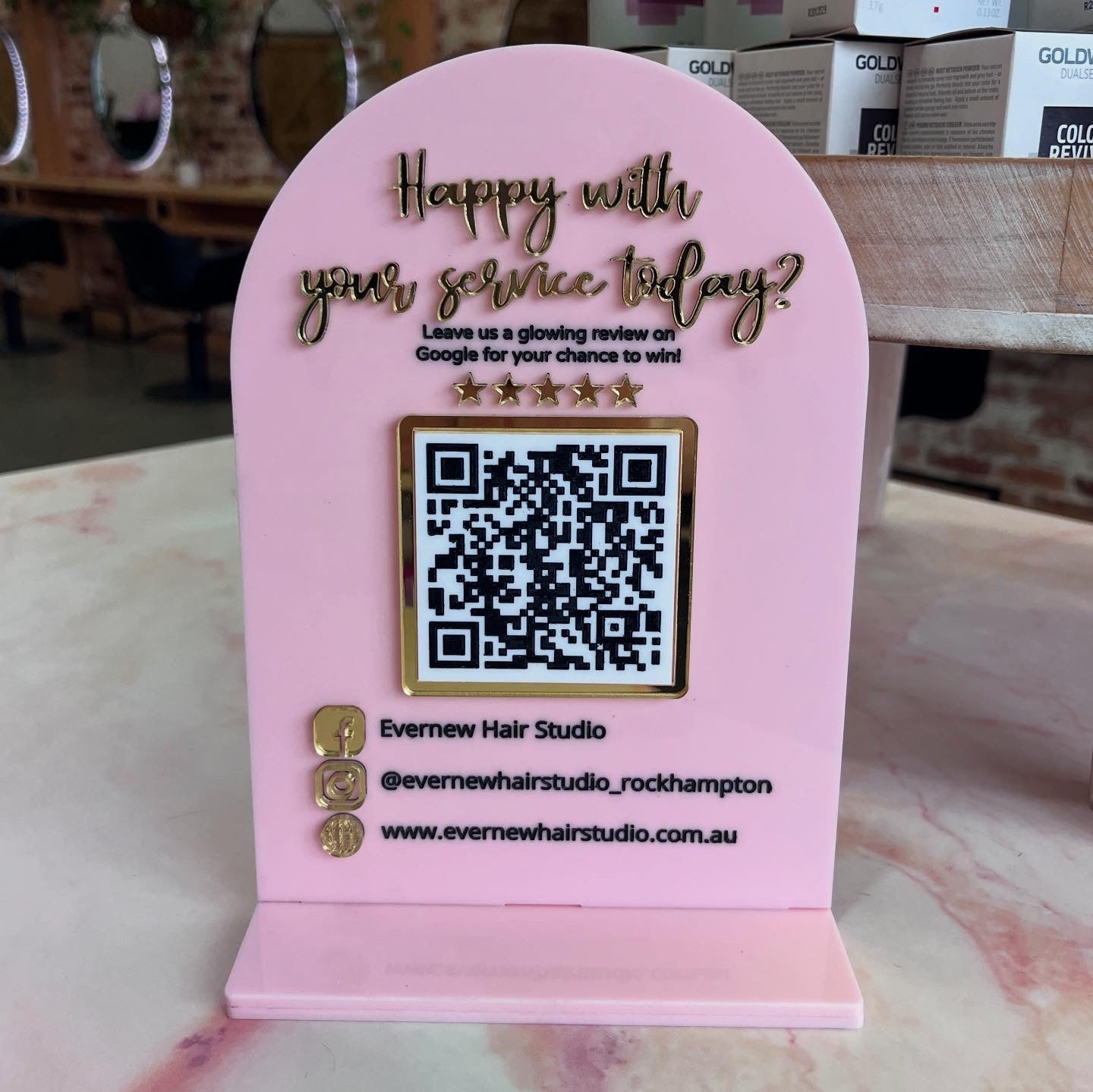 Pink sign with QR code and text on a table, likely at a hair salon.