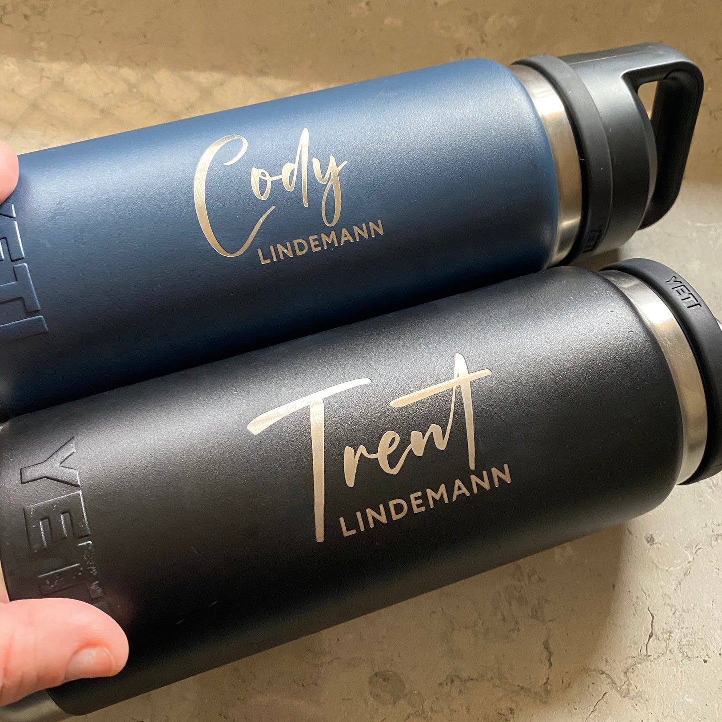 Two YETI brand tumblers with personalized name engraving on a beige surface.