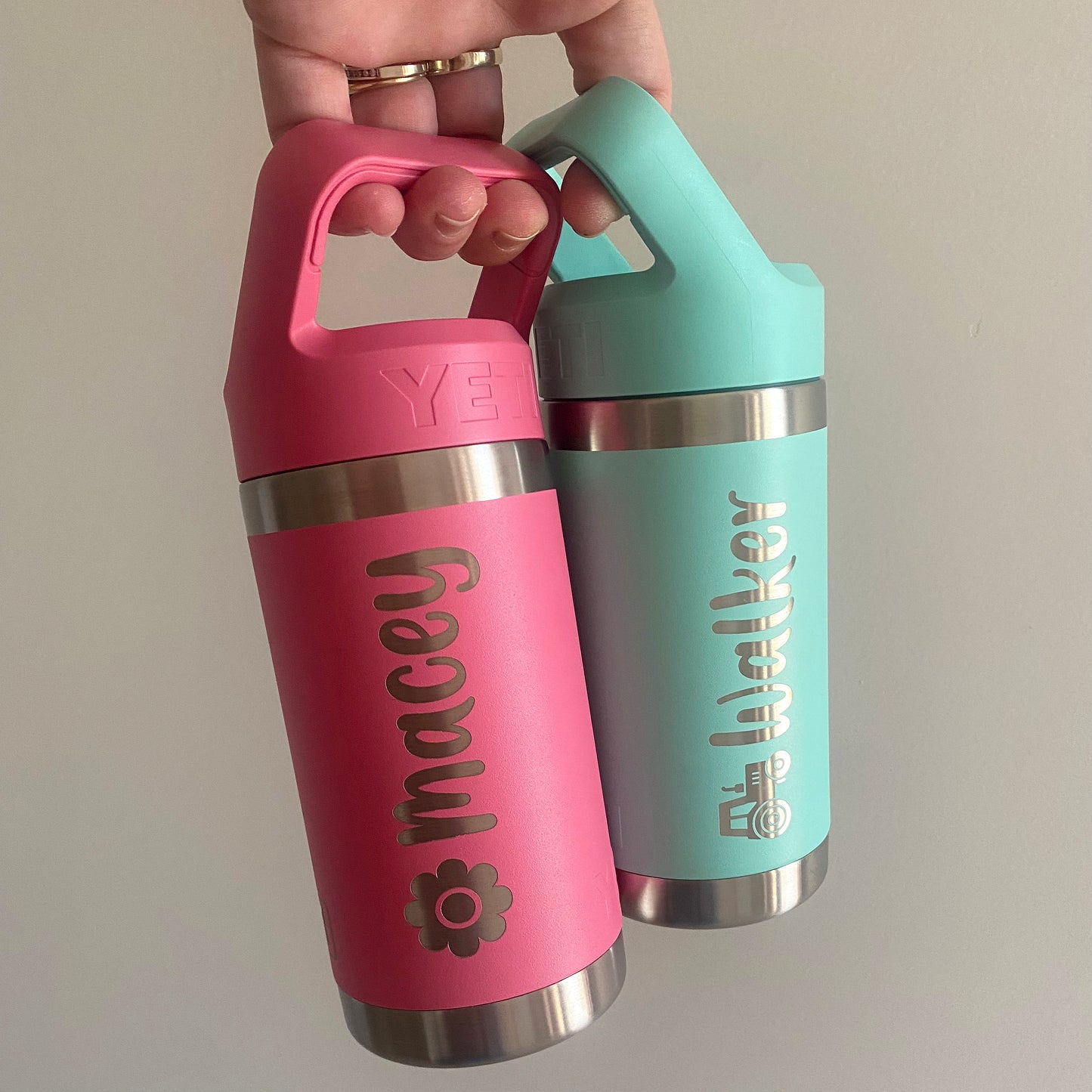 Two colorful water bottles with engraved names held by a hand against a plain background.