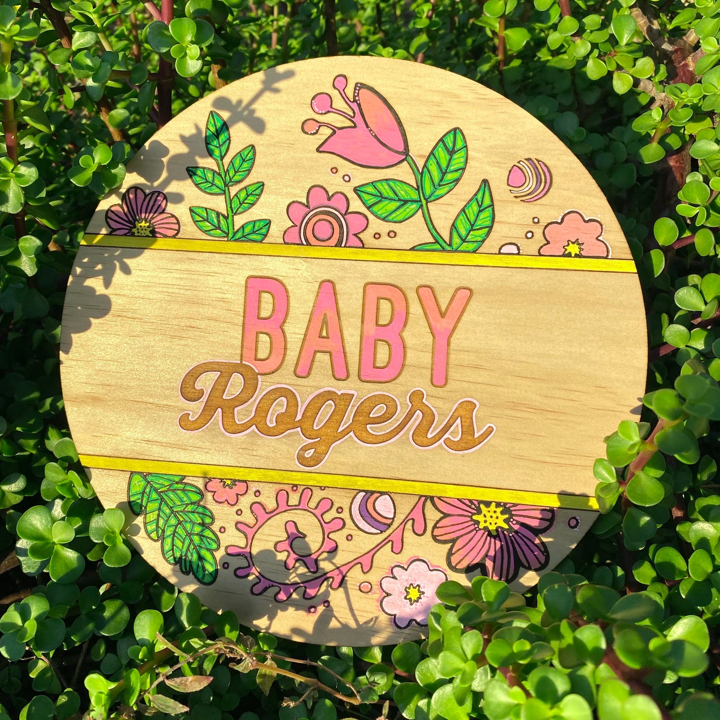 Wooden plaque with floral designs and 'Baby Rogers' text on a green leaf background