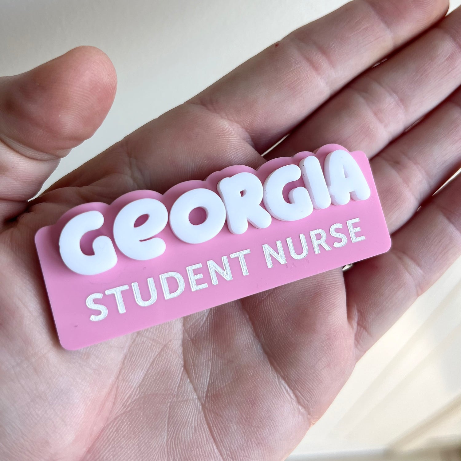 A name badge with the name Georgia  'Student Nurse' held on a palm against a neutral background.