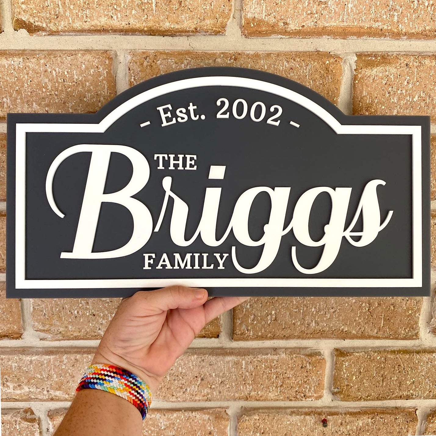 Custom acrylic family name sign, established year and surname. Held in front of a brick wall.